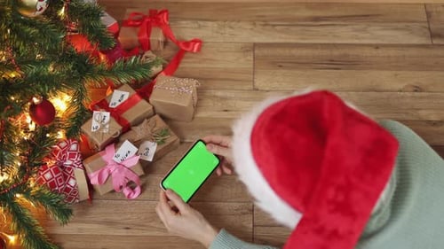 Female Red Christmas Hat Smartphone Hands Green Screen Under Fir Tree Gift Boxes