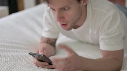 Young Adult Using Smartphone Lying on Bed