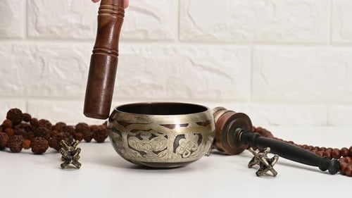Hand Demonstrates Singing Bowl with Beads and Drumsticks