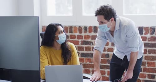 Man and woman wearing face masks working together in office