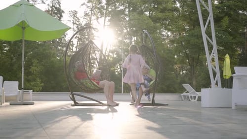Old Couple Sitting on a Hanging Chair on the Sunset, Relaxing in the Hotel Complex Together