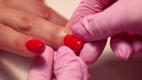 Die Hände des Meisters in Handschuhen im Schönheitssalon untersuchen die Nägel und die Nagelhaut nach dem Färben rot