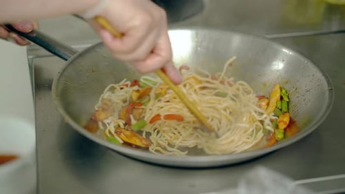Gloved Person Stir Frying Noodles and Vegetables