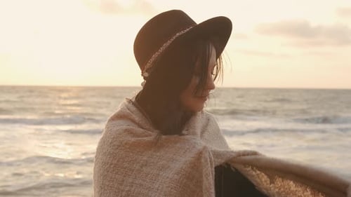 Portrait of Romantic Brunette Woman in Hat and Coat Walking on the Beach in Autumn at Sunset or
