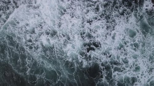 Luftaufnahme von oben nach unten von riesigen Meereswellen, die am Korallenstrand krachen und schäumen