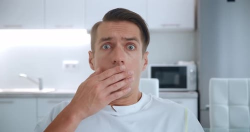Man covers mouth in shock and surprise indoors