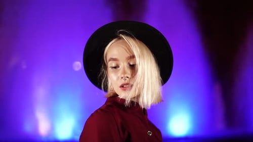 Portrait of Millennial Hipster Woman with Blond Hairstyle Standing on Neon Fountain Background. City