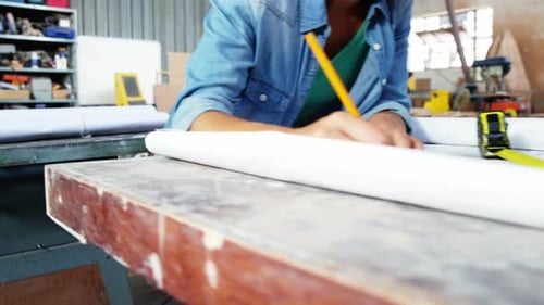 Woman Studies Blueprint with Pencil in Workshop