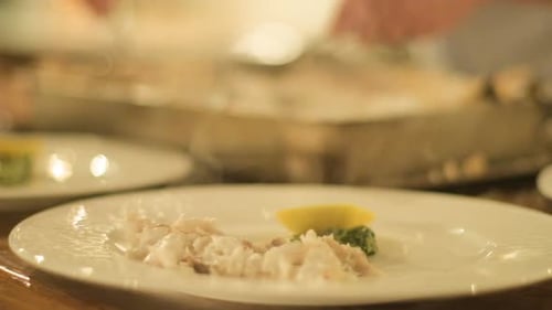 Chef preparing and decorating fish, many round plates with meal in kitchen in restaurant