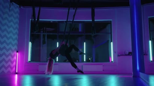 Woman Performs Aerial Yoga in Neon Lit Studio