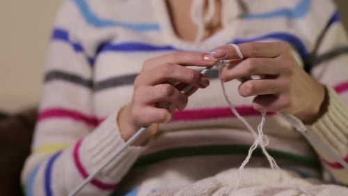 Hands Knitting with White Yarn and Needles