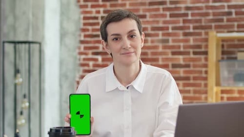 Nice Woman in White Shirt Shows the Phone with the App Sitting in Office and Looking at Camera