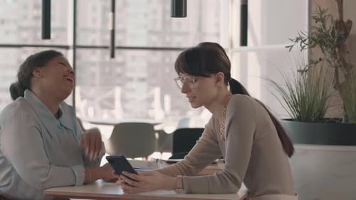 Diverse Female Colleagues Looking at Smartphone and Talking in Cafe