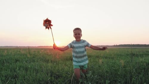 Menino criança correndo com um moinho de vento de brinquedo em um campo no verão ao pôr do sol