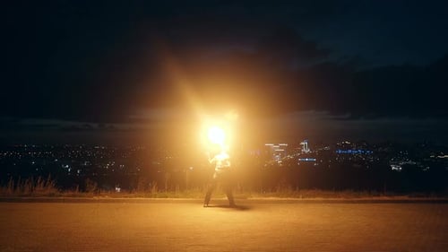 Shirtless Man Juggling Fire in Front of City
