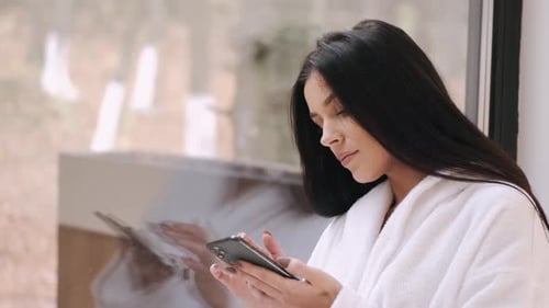 Woman in Robe Using Phone by Window
