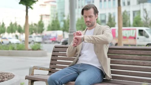 Man Sits on Bench Using Smart Watch in City