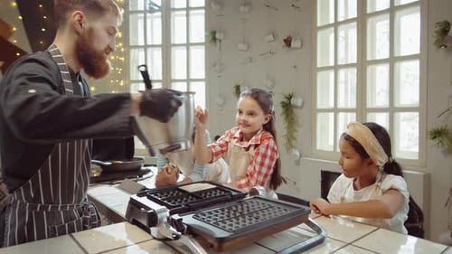 Niños que aprenden a cocinar gofres en una clase de cocina con el chef