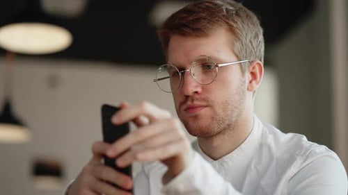 Attractive Man Glasses Standing Alone Indoor Holding in Hands Smart Phone Dial Number on Touchscreen