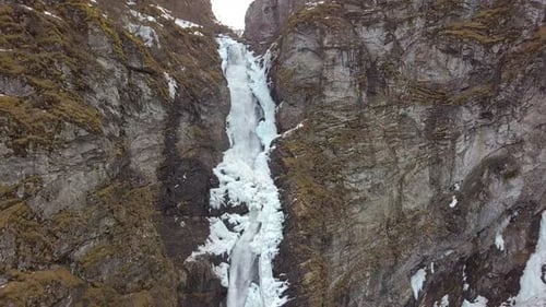 Luftaufnahme eines eisigen Wasserfalls, der durch eine Klippe in Norwegen schneidet, langsame Abstiegsbewegung