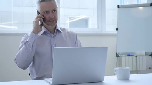 Man Talking on Phone Working at Laptop
