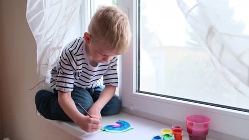 Boy Carefully Painting a Picture on Window Sill