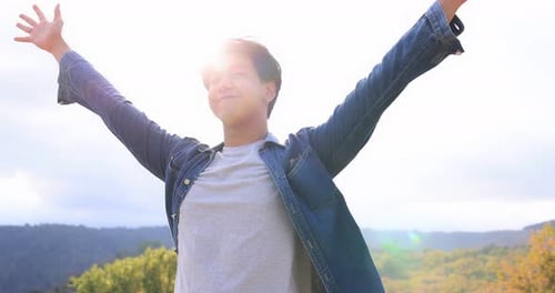 Freedom Asian young man raising hands on the top at the mountain.
