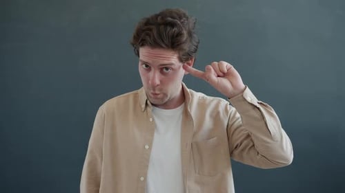 Emotionaler junger Mann zeigt Bist du verrückt Handgeste Finger in der Nähe des Kopfes drehen und anschauen