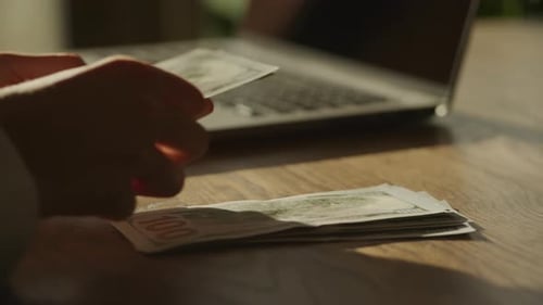 Handheld Closee Up of Caucasian Woman Hands Counting Money Dollar Bill in Front of Laptop Computer