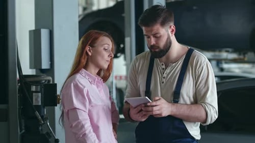 Woman and Mechanic Discuss Car Repairs Using Tablet