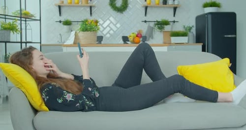 Beautiful Young Woman Holding a Smartphone in Hands and Typing on Its Screen While Chatting