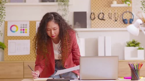 Young entrepreneur using laptop writing notes standing at home office desk. Young business woman pro