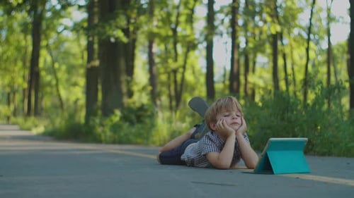 Preschool Boy Using Tablet Computer Laying on the Ground in Park. Kid Watching Gadget Online Outside