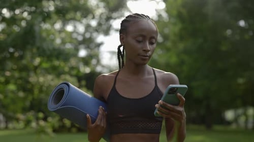 Woman Holding Yoga Mat and Using Smartphone in Park