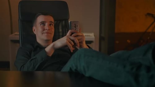 Man Relaxing in Office Chair Looking at Phone