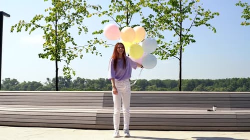 Happy Redhead Young Woman Carefree Playing and Jumping with Large Fountain of Colorful Balloons.