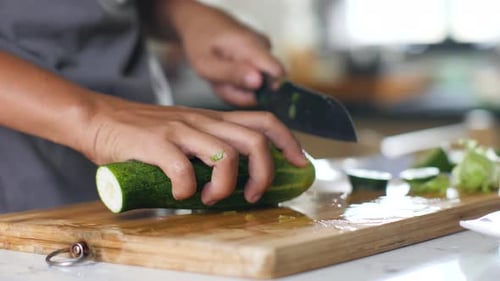Close Up of Woman's Hands Slicing Ca Fresh Cucumber on a Wooden Cutting Board.
