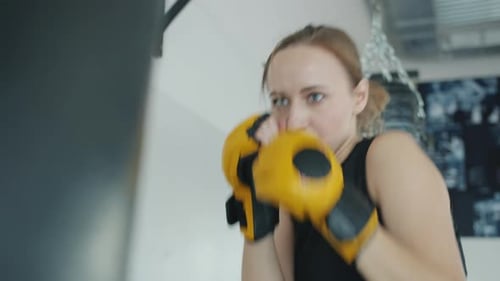 Strong Female Kickboxer Training with Punching Bag Indoors in Gym Exercising Alone