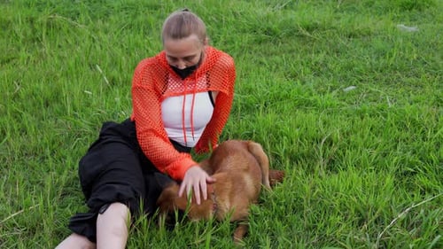 A Young Blonde Woman with a Braid Wearing an Orange Hoodie with a Mask on Her Face Plays on the
