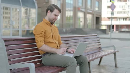 Man Using Laptop on City Bench Celebrates Success