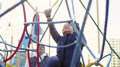 Happy Caucasian Boy Climbing on Net Structure in Playground