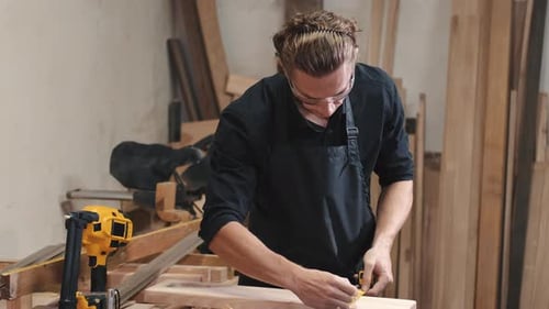 Carpenter with Ruler Measuring Plank at Workshop