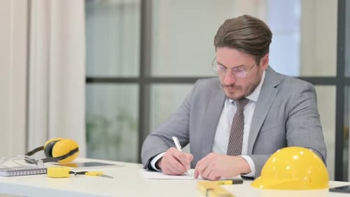 Engineer Writing at Desk With Hard Hat