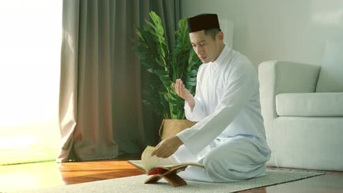 Man Praying Indoors in White Robe with Book