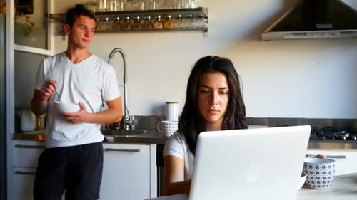 Woman Uses Laptop as Man Eats Breakfast in Kitchen