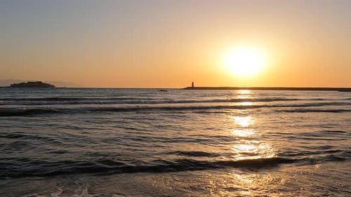 Zeitlupenaufnahme auf Meereswellen am Strand mit Leuchtturm und Inselblick bei Sonnenuntergang