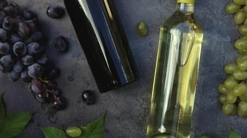 Blick von oben auf Flasche Rot- und Weißwein, grüne Weinrebe, Weinglas und reife Traube auf dunklem Vintage-Stein