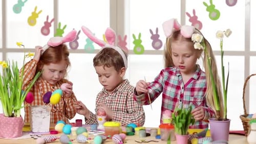 Glückliche Kinder tragen Hasenohren beim Eiermalen am Ostertag