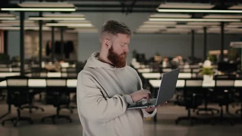 Bearded Man Using Laptop Working On Computer Standing In Office
