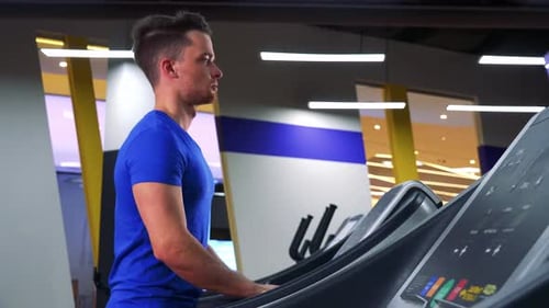 A Young Fit Man Walks on a Treadmill in a Gym - View From Side